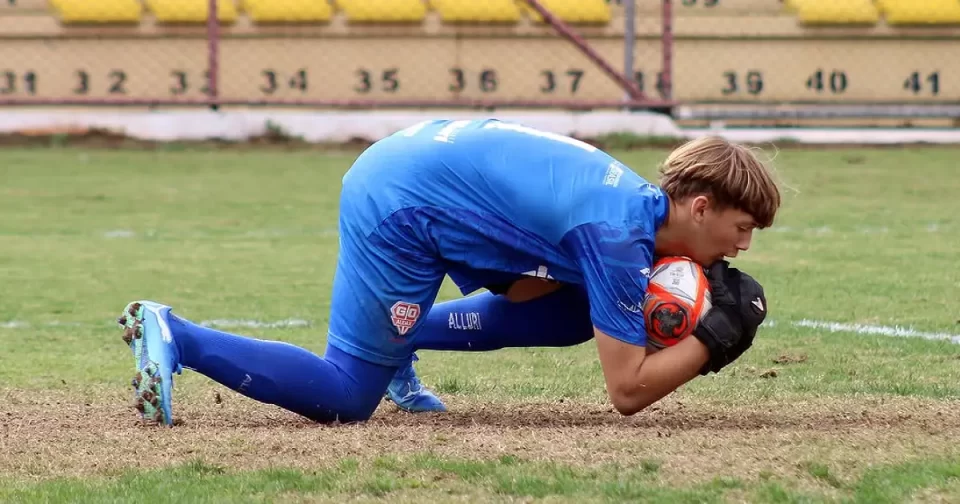Goleiro usando uniforme azul, encaixa bola durante jogo do Campeonato Paulista Sub 15.